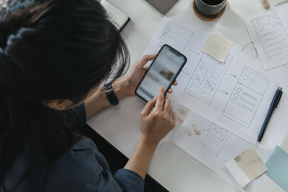 A participant testing a phone prototype beside paper layouts
